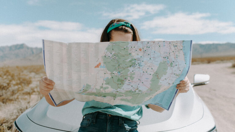 woman on side of the road in the desert leaning on the hood of her car reading a large map